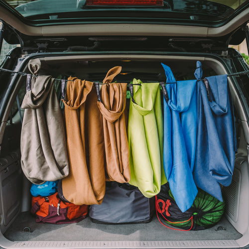 Image of multiple Gear Aid microfiber towels hanging to dry inside an open vehicle trunk, assorted fabric colors in outdoor travel use, rear lifestyle view.
