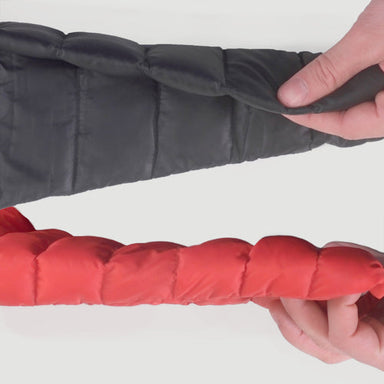 Image of two insulated jacket sleeves being held and compared by hands, one black and one red, showing quilted padding thickness and loft, close-up view on white background.