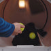 Image of a hand placing yellow dryer balls into a tumble dryer with a dark insulated jacket inside, interior drum view showing laundry care process.