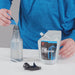 Image of Gear Aid Revivex Odor Eliminator being transferred from a flexible pouch into a clear spray bottle using a blue measuring cap, with spray nozzle beside it, tabletop setup on neutral background.