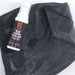 Image of Gear Aid Seam Grip TF Tent Fabric Sealant bottle placed on worn black tent fabric with visible scuffs, top-down view showing repair context on white background.