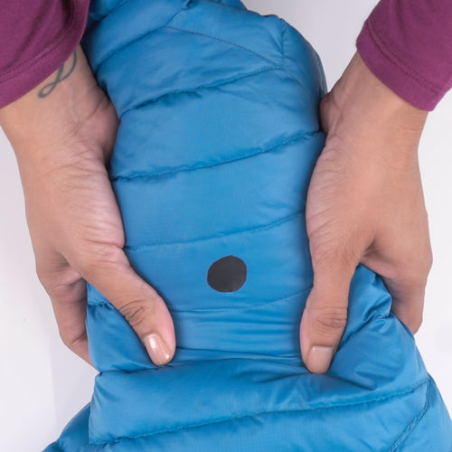 Image of hands holding a blue insulated jacket sleeve with a round black repair patch applied, close-up front view showing completed fabric repair on white background.