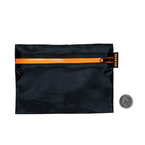 Image of compact black zippered gear pouch with orange waterproof zipper and logo tag, flat front view with a coin for size reference on a white background.
