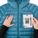 Image of Gear Aid Tenacious Tape Mini Patches demonstrated on a blue down jacket with hands smoothing fabric and retail packaging shown, front-facing repair example on white background.