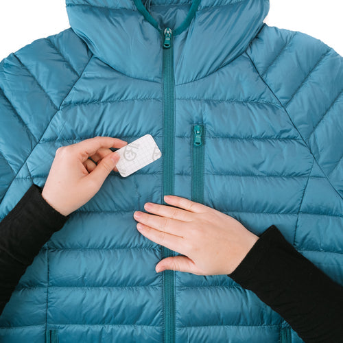Image of Gear Aid Tenacious Tape Mini Patch being positioned by hand over a tear on a blue down jacket, close-up repair step shown on white background.
