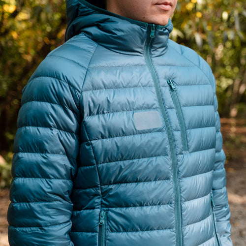 Image of a blue down jacket worn outdoors after repair with Gear Aid Tenacious Tape Mini Patch, showing a smooth, reinforced area on the chest, angled front view in natural setting.