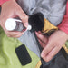 Image of hands applying Gear Aid zipper cleaner and lubricant to a jacket zipper using brush applicator, close-up action view on outdoor fabric background.