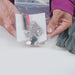 Image of hands holding a clear zip bag containing zipper repair kit components including metal sliders and needle tool, front view on white background.