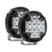 Image of two round, black LED off-road lights, each with a square array of four clear light reflectors, mounted on silver U-shaped brackets, on a white background. The lights are positioned at a slight angle, with one slightly behind the other.