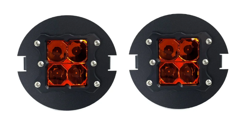 Pair of round black off-road lights with amber lenses, featuring four square LED lights each, shown on a white background.