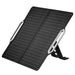 An image of a portable, foldable solar panel, black in color with thin white lines indicating the solar cells, angled upwards as if deployed with its integrated stand. The panel has two light grey, possibly metallic, elongated oval-shaped handles or supports on either side. The background is white