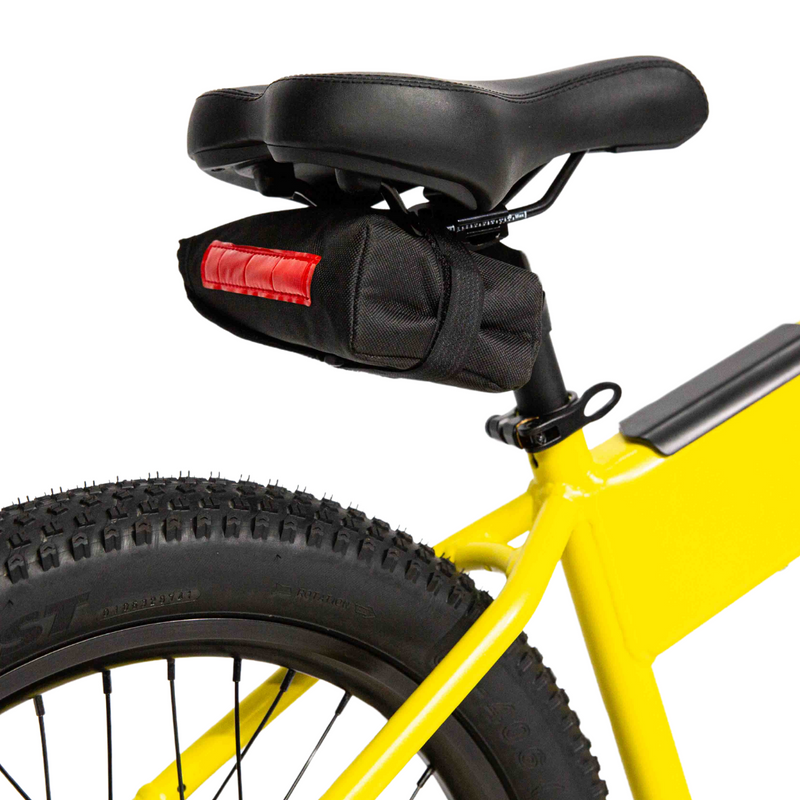 Image of black fabric saddlebag with red reflective strip securely mounted under the seat of a yellow bicycle, close-up rear side view on a white background.