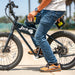 Image of a person sitting on a black JackRabbit fat-tire electric bike, holding an extra battery pack in their hands on a paved road.