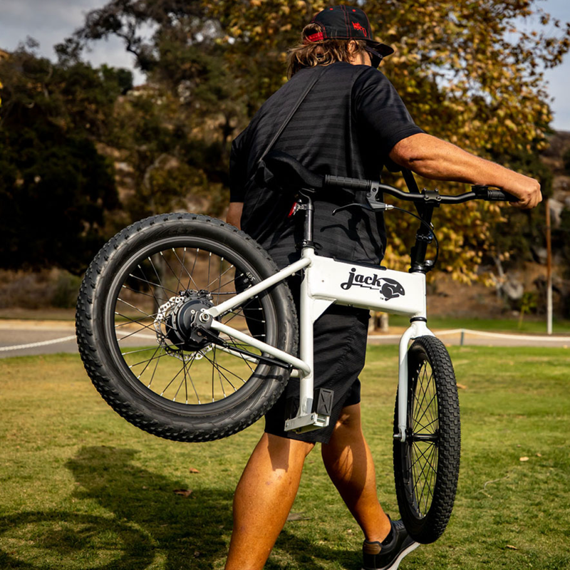 Image of JackRabbit electric bike with shoulder carry sling, compact white frame with black tires, side view being carried outdoors on grassy park background.