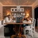 Image of Jackery Explorer 2000 portable power station placed on a dining table powering devices, black and orange unit with connected cables in use by a family, straight-on front view in indoor home dining setting.