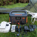 Image of Jackery Explorer 500 portable power station at a campsite, front view on grass powering drone batteries and electronic devices with tent and drone visible in the background.