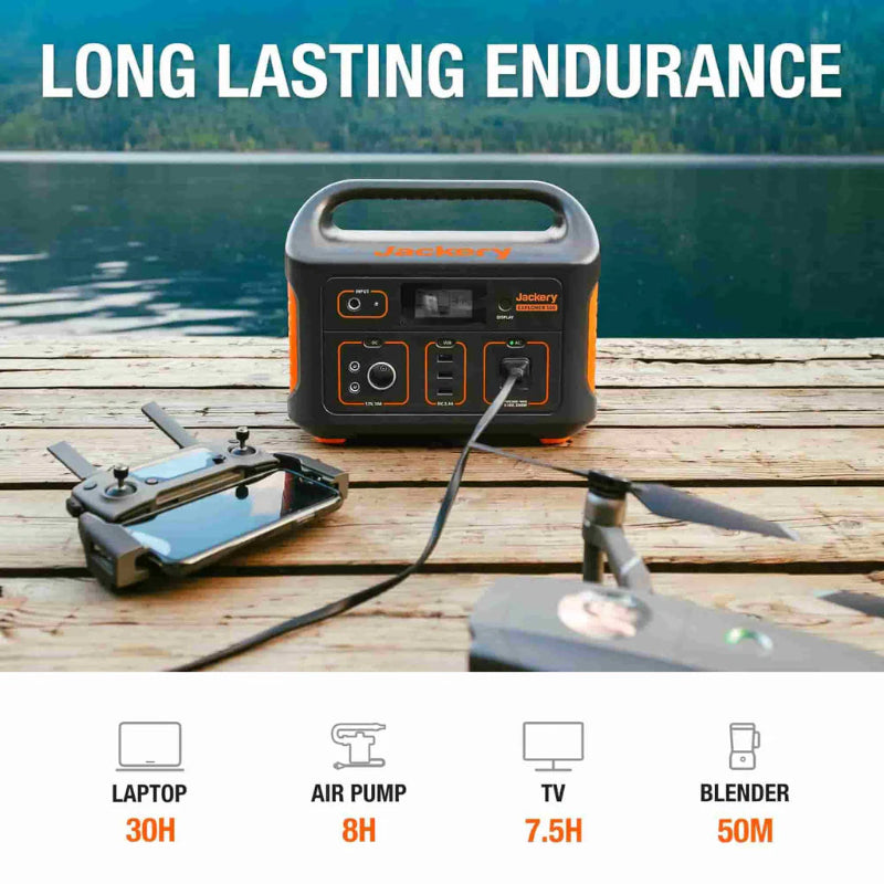 Image of Jackery Explorer 500 portable power station in outdoor camping setup on a wooden table by a lake, connected to electronic devices, front view with handle visible and endurance usage icons below.