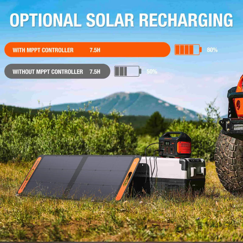 Image of Jackery Explorer 500 portable power station outdoors with optional solar panel recharging setup, angled side view showing connected solar panels and power unit on grassy terrain with mountains in the background.