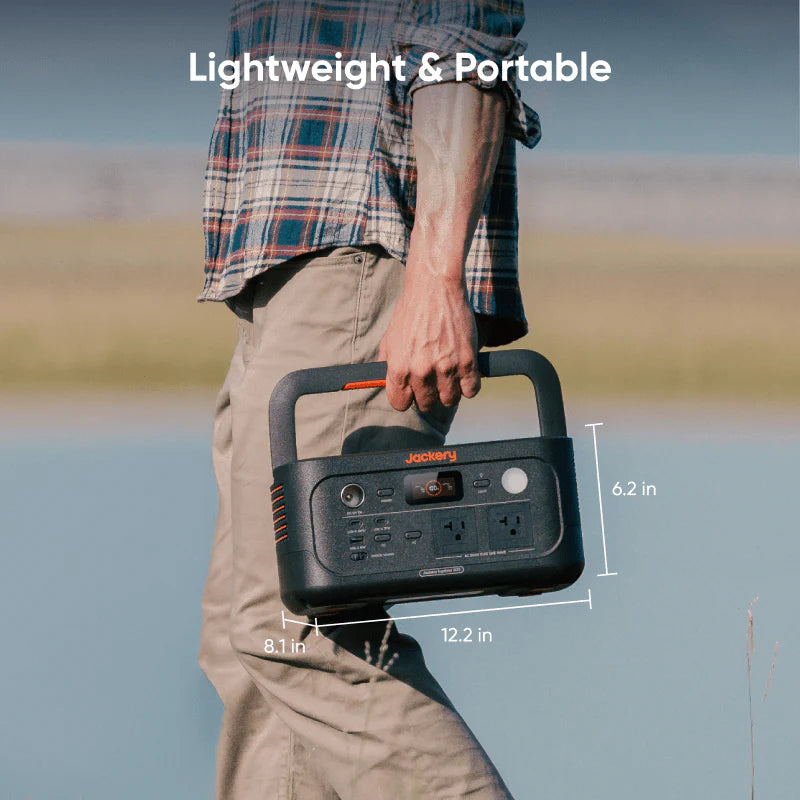 Image of Jackery Explorer 600 portable power station being carried by hand, compact dark gray unit with orange accents and built-in handle, lifestyle outdoor scene with size dimensions overlaid on the image.
