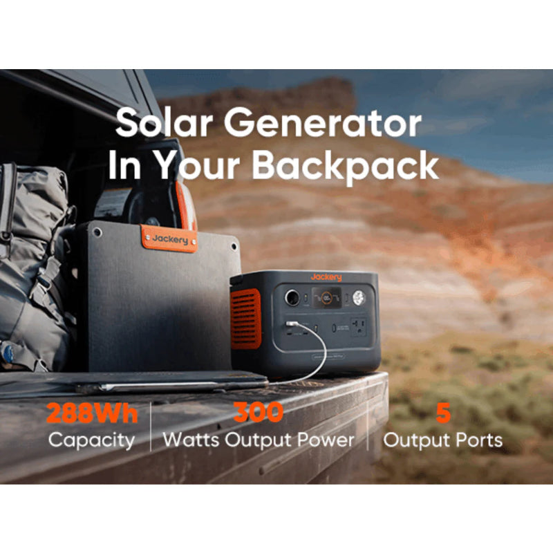 Image of a Jackery portable power station and foldable solar panel placed on a vehicle tailgate during outdoor travel, black and gray units with orange accents, angled front view in a desert landscape setting.