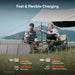 Image of a Jackery portable power station and foldable solar panels being used at an outdoor campsite under a canopy, black and gray units with orange accents, front view in a grassy lakeside setting with charging time icons displayed.
