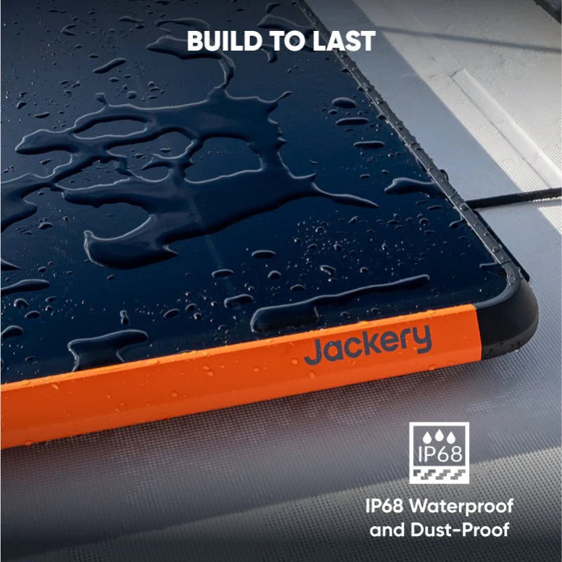 Image of Jackery SolarSaga 100 Prime solar panel close-up showing water droplets on black surface with orange trim, highlighting IP68 waterproof and dustproof build, angled detail view on outdoor surface.