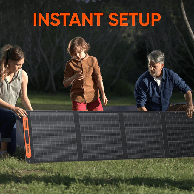 Image of a Jackery portable foldable solar panel being set up outdoors by two adults and a child on grass, black photovoltaic panels with orange accents, front view in a natural outdoor setting.