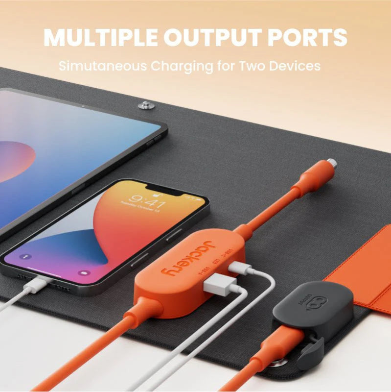 Image of Jackery SolarSaga 40W Mini solar panel output hub with multiple charging ports powering a smartphone and tablet, black panel surface with orange connectors, angled top view on neutral background.