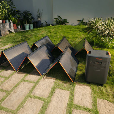 Image of multiple Jackery foldable portable solar panels arranged in a zigzag layout and connected to a Jackery power station, black photovoltaic panels with orange trim, angled front view on a grassy backyard setting.