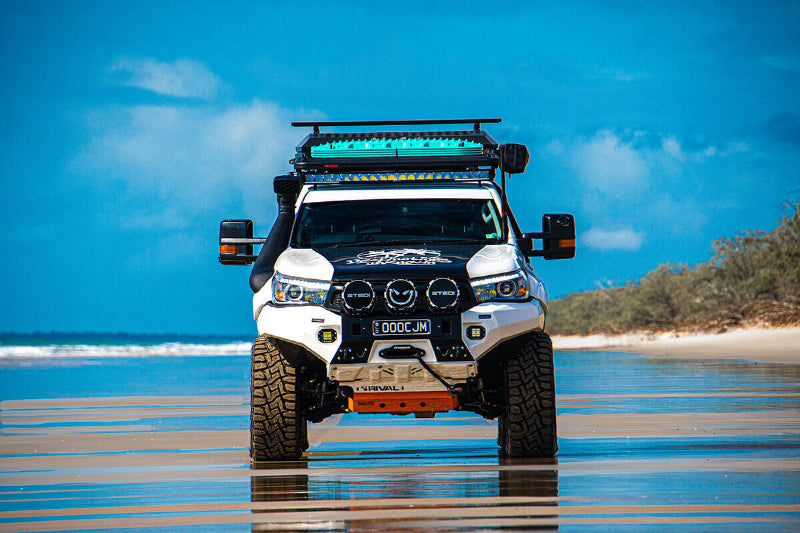 Image of off-road 4WD vehicle driving on beach with teal MAXTRAX MKII recovery boards mounted on roof rack, front view with ocean and sky background.