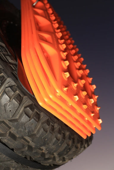 Close-up image of stacked orange MAXTRAX MKII recovery tracks mounted to a spare tire, viewed from a low angle against a dark sky.