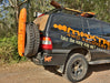Black 4x4 vehicle with "MAXTRAX 4WD RECOVERY" decal, featuring orange MAXTRAX recovery boards mounted on the rear spare tire and a shovel on the roof rack, parked outdoors.