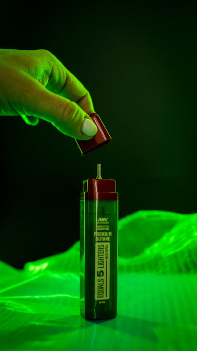 Image of MK Outdoor premium butane lighter refill 20ml with red cap removed, green canister upright with nozzle exposed, close-up front view against dark green background.
