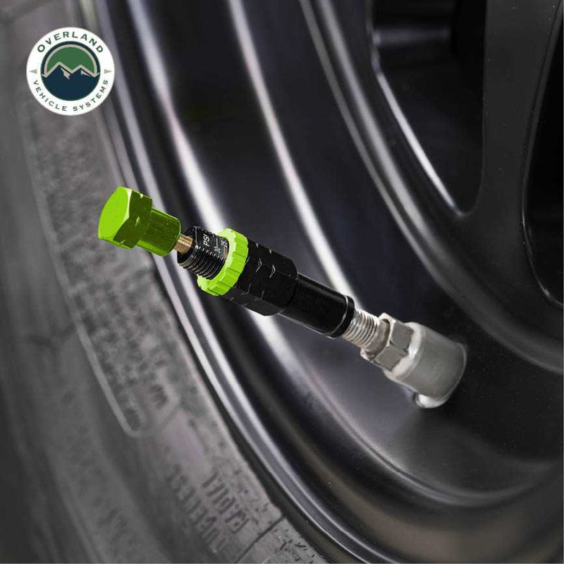Image of an Up Down Air tire deflator with a green cap and black body, attached to a tire valve stem on a black vehicle rim, on a white background with the "Overland Vehicle Systems" logo.