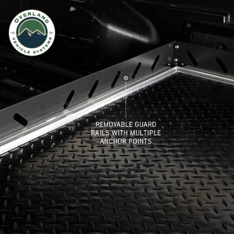 Image of Overland Vehicle Systems truck bed extension with diamond plate surface, showing removable guard rails with multiple anchor points, close-up view of the rail system