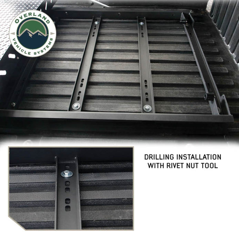 Image of Overland Vehicle Systems truck bed extension with drilling installation, showing rivet nut tool and mounting rails, close-up view with text overlay highlighting the installation proces
