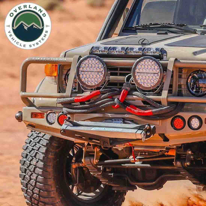 Image of off-road vehicle front bumper equipped with Overland Vehicle Systems kinetic recovery rope and winch, black braided rope with red reinforced loops mounted on rugged 4x4 truck in desert terrain, front angled view.