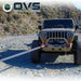 Image of OVS Brute Recovery Tow Strap in use during an off-road vehicle recovery, gray synthetic strap attached to a Jeep front bumper on a rocky trail, front view in outdoor setting.