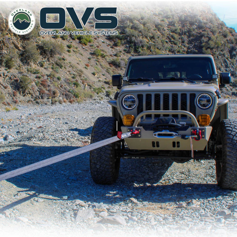 Image of OVS Brute Recovery Tow Strap in use during an off-road vehicle recovery, gray synthetic strap attached to a Jeep front bumper on a rocky trail, front view in outdoor setting.