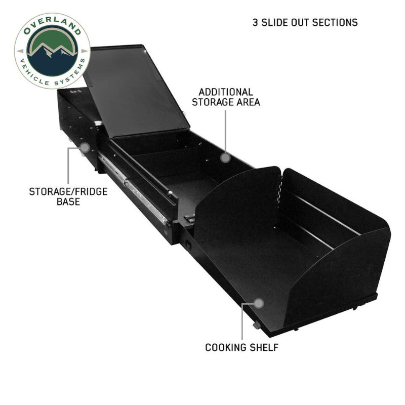 Image of an Overland Vehicle Systems (OVS) Cargo Box Cooking Station, fully extended to show all three slide-out sections, labeled "STORAGE/FRIDGE BASE," "ADDITIONAL STORAGE AREA," and "COOKING SHELF." The cooking station is black and shown from a front-side angle on a white background