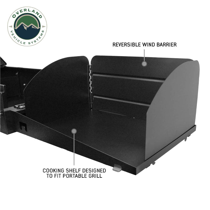 Image of an Overland Vehicle Systems (OVS) Cargo Box Cooking Station, with the cooking shelf fully extended and a reversible wind barrier set up. The image highlights the "COOKING SHELF DESIGNED TO FIT PORTABLE GRILL" and "REVERSIBLE WIND BARRIER" on a white background