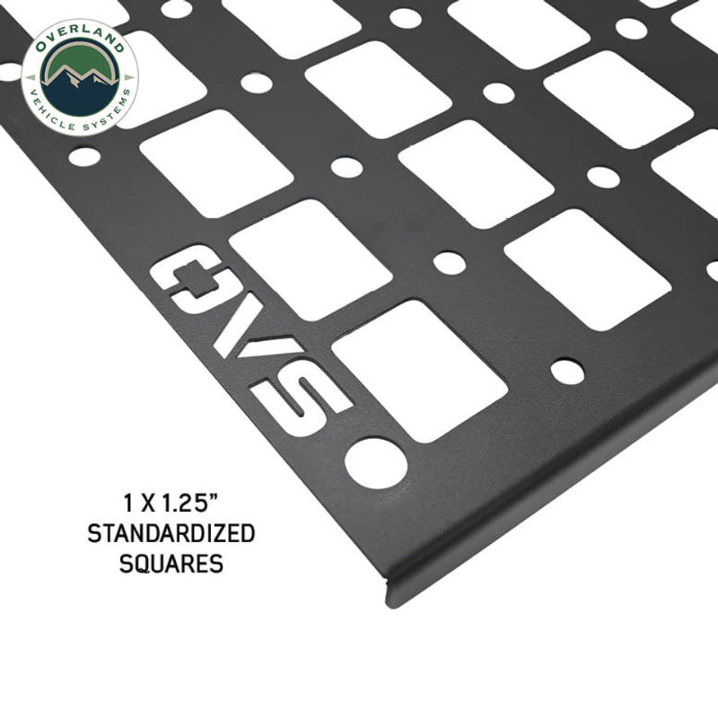 Image of a black metal MOLLE panel with "OVS" prominently displayed, highlighting the 1x1.25" standardized square cutouts. The Overland Vehicle Systems logo is visible in the top left corner, with the panel shown at an angle on a white background