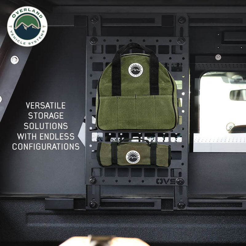 Image of a black MOLLE panel installed inside a vehicle, showcasing its versatile storage capabilities with two green Overland Vehicle Systems bags attached. The panel is mounted vertically, with the vehicle's interior visible around it