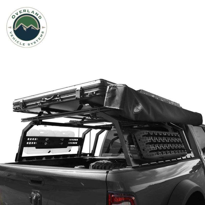 Image of Overland Vehicle Systems roof rack mounted on a truck with rooftop tent and mounted recovery ramps, side view with black fabric awning and visible storage options, on a white background