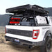 Image of Overland Vehicle Systems roof rack mounted on a Ford Raptor truck, featuring a rooftop tent, fuel canisters, and storage boxes in the truck bed, with a scenic background