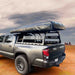 Image of the black OVS Discovery Rack with a rooftop tent mounted on top, shown from an angled side and rear view on a gray pickup truck in a rugged desert landscape