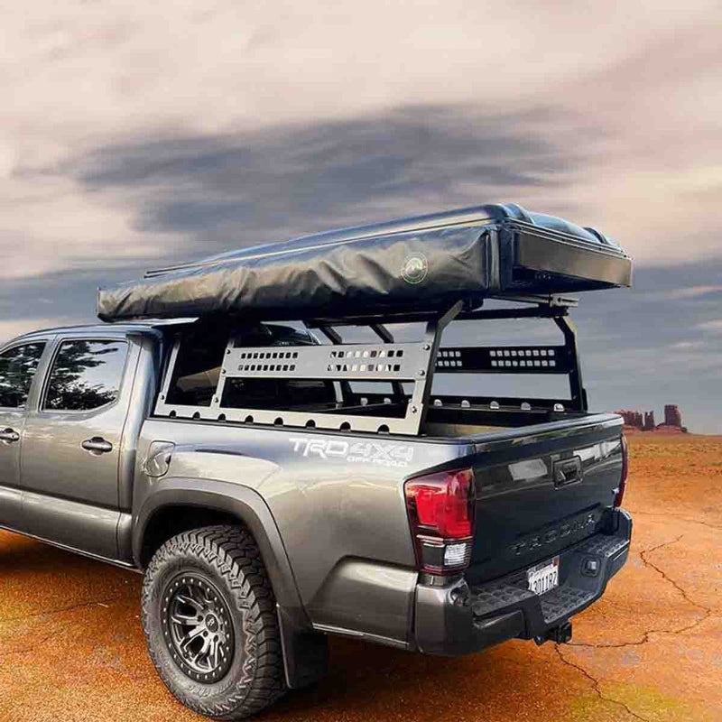 Image of the black OVS Discovery Rack with a rooftop tent mounted on top, shown from an angled side and rear view on a gray pickup truck in a rugged desert landscape