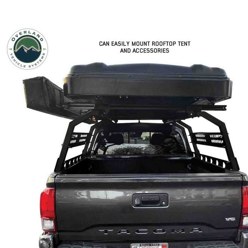 Image from a rear view of a gray pickup truck equipped with the black OVS Discovery Rack, which securely mounts a closed black rooftop tent and an attached awning