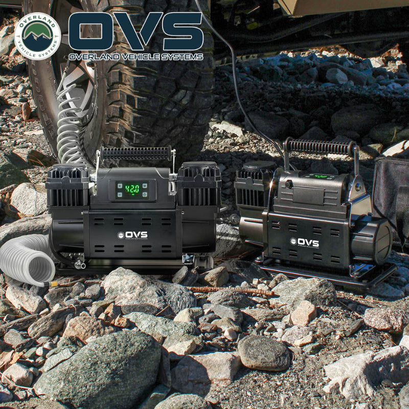 Image of OVS portable digital air compressors in use during off-road tire inflation, black units with digital displays and coiled hoses, placed on rocky terrain beside a vehicle tire in an outdoor setting.