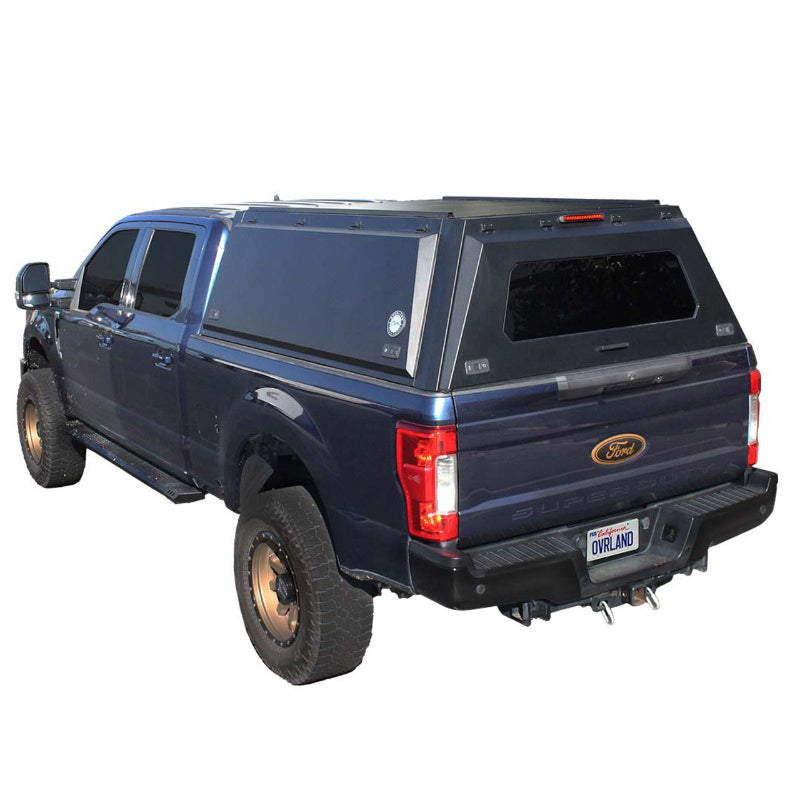 Image of a dark blue Ford Super Duty truck with a black truck bed cap installed. The cap features side access doors and a rear window, shown from a rear three-quarter view on a white background